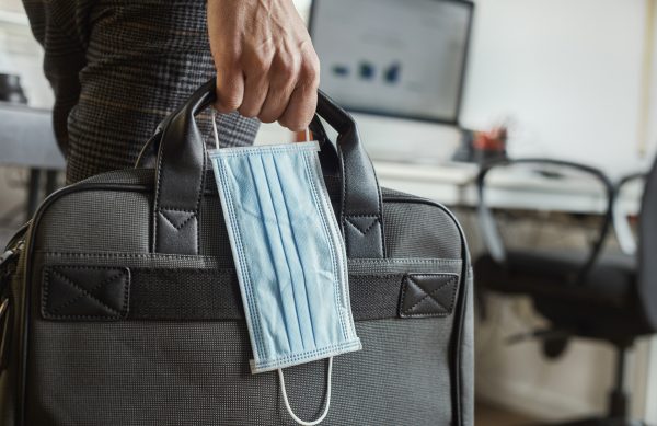 closeup of a young man in an office holding a briefcase and a surgical mask in his hand